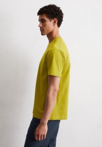 Koszulka z krótkim rękawem w jasnym limonkowym kolorze, wykonana z bawełny. Standardowy krój z okrągłym dekoltem i prostymi szwami.