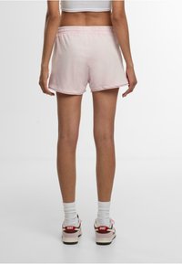 Shorts en coton rose avec une taille élastique, ourlet roulé et coupe décontractée, portés avec des chaussettes blanches et des baskets rouges et blanches.