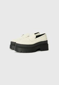 Mocassins en cuir blanc avec une semelle plateforme noire épaisse, présentant un bord surélevé et des détails de couture subtils.