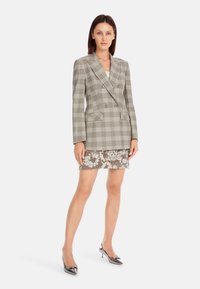 Gestrickte, graue und weiße, doppelte Blazerjacke über einem gemusterten Spitzen-Minirock. Silbern spitze High Heels runden das Outfit ab.