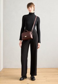 Braune Lederhandtasche mit strukturierter Form, glatter Textur und einem goldenen Akzent auf der Vorderseite. Trägt man zu einem schwarzen Rollkragenpullover und weit geschnittenen Hosen.
