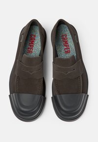 Hnědé semišové slip-on boty s kulatou špičkou z černé gumy. Interiér má texturovanou stélku s červeným nápisem "Camper".