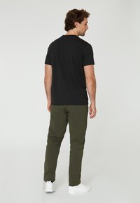 Svart kortärmad t-shirt för män med rund halsringning, i kombination med olivgröna byxor och vita sneakers, sedd bakifrån.