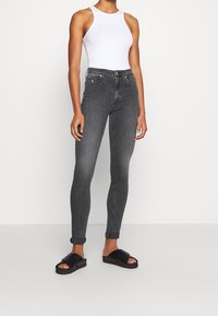Vaqueros gris de corte slim con puños enrollados, combinados con una blusa sin mangas blanca y sandalias negras de tiras. Textura de denim suave.
