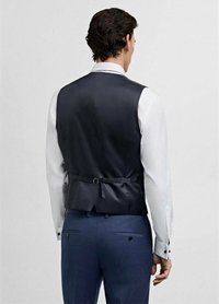 Gilet marine avec une texture lisse, doté d'une boucle dans le dos et d'une coupe ajustée, associé à une chemise blanche à manches longues et un pantalon bleu.