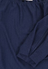 Navy textiel met een gekreukt patroon. Kenmerkt zich door een elastische halslijn en mouwen, wat een zachte, gedrapeerde uitstraling geeft.