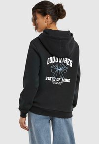 Hoodie noir avec une poche kangourou à l'avant, présentant un texte blanc et un graphique floral bleu clair à l'arrière. Fabriqué en tissu doux avec des poignets côtelés.