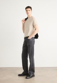 Beige rövidujjú kötött póló, sötét szürke egyenes szabású farmer, fekete cipők és egy fekete dzseki, amit az egyik vállára terített.