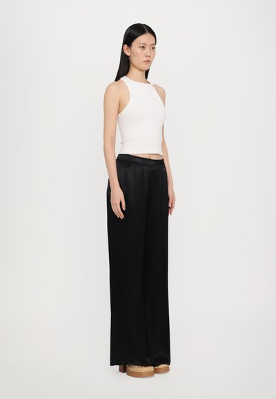 Top court sans manches blanc associé à un pantalon ample en satin noir avec une taille élastique, porté avec des chaussures à plateforme en bois épaisses.