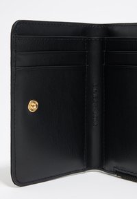 Interior de cartera de cuero negro con múltiples ranuras para tarjetas, acabado texturizado y detalle de emblema dorado. Los bordes cosidos proporcionan durabilidad.