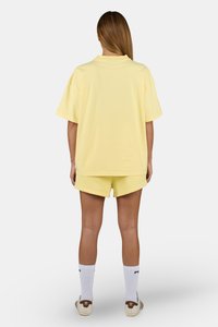 Gul oversized t-skjorte og matchende shorts laget av bomull, med en avslappet passform. Hvite sokker og lyse sko fullfører antrekket.