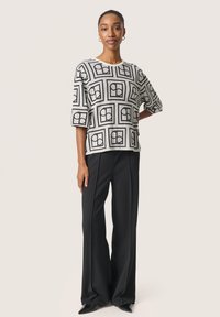 Hvid og sort mønstret top med geometrisk design, parret med højtaljede sorte bukser og spidse sorte sko.