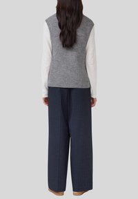 Grijze gebreide vest met een gestructureerde afwerking, gedragen over een witte blouse met lange mouwen, gecombineerd met brede blauw gestreepte broek.