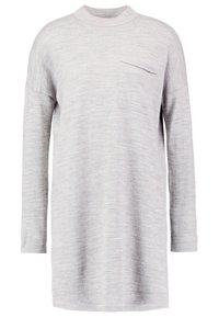 Tunique tricotée à manches longues de couleur gris clair avec col montant et petite poche poitrine, présentant une coupe décontractée et un tissu doux et texturé.