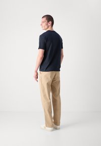Marineblå kortærmet T-shirt parret med beige bukser. T-shirten har en rund halsudskæring, og bukserne har en afslappet pasform og sidelommer.