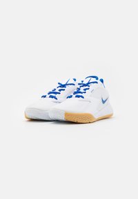 White athletic shoes with blue accents and laces. Features a textured, rubber outsole and smooth upper material. Nike logo on the side.