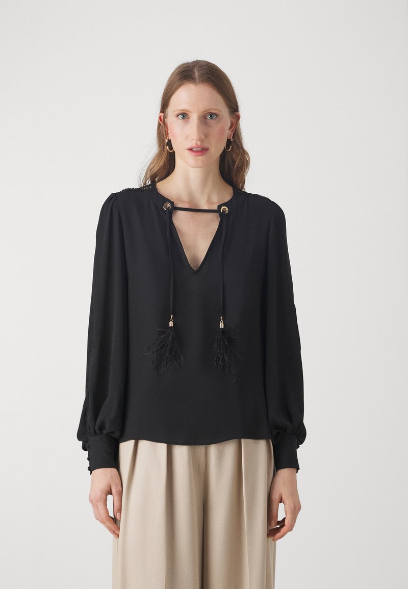 Black blouse with a V-neckline, featuring a tie with feather tassels. Long sleeves with gathered cuffs. Smooth fabric with subtle sheen.