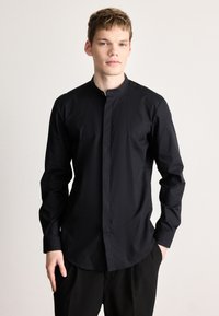 Fekete hosszú ujjú ing álló gallérral és gombos előlappal. Simább, könnyű anyagból készült, szabott fazonú és letisztult dizájnnal.