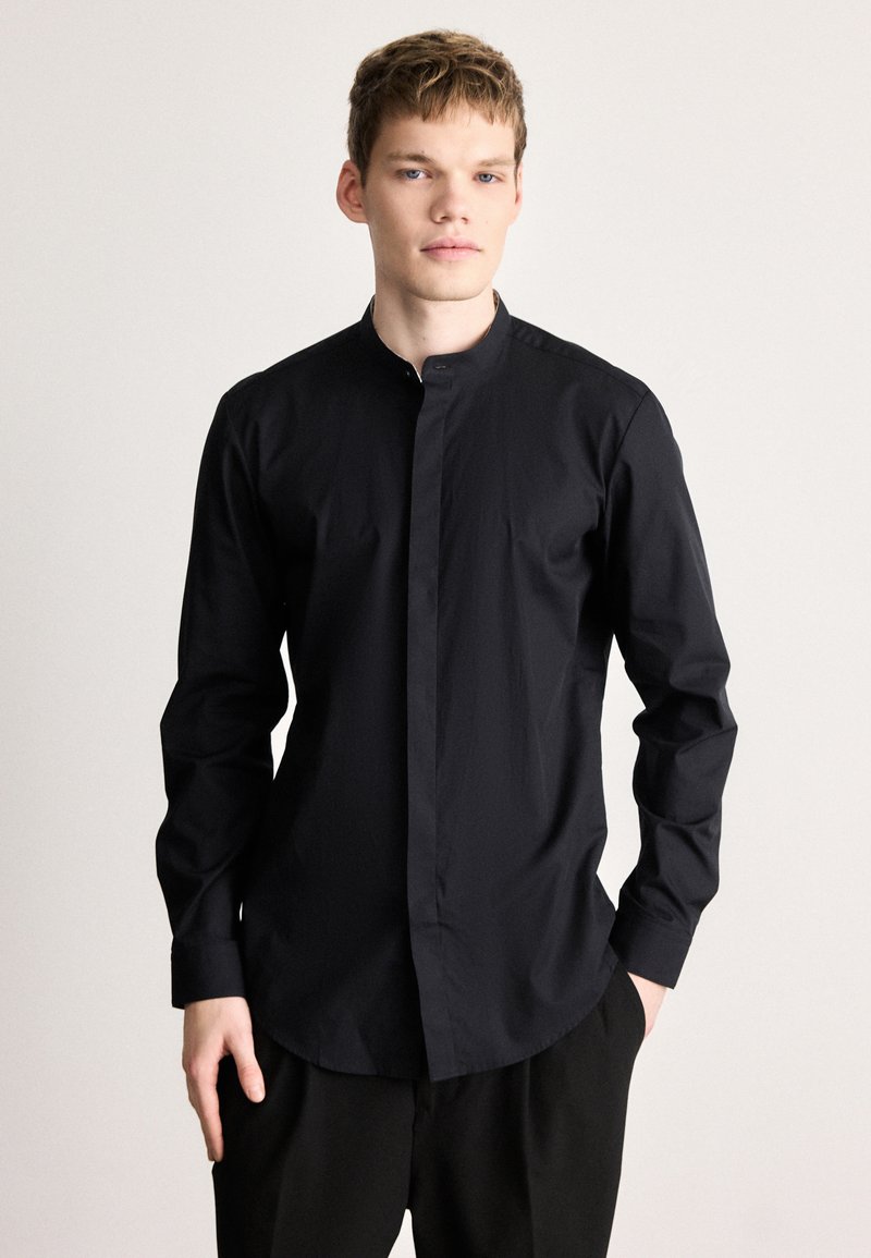 Fekete hosszú ujjú ing álló gallérral és gombos előlappal. Simább, könnyű anyagból készült, szabott fazonú és letisztult dizájnnal.