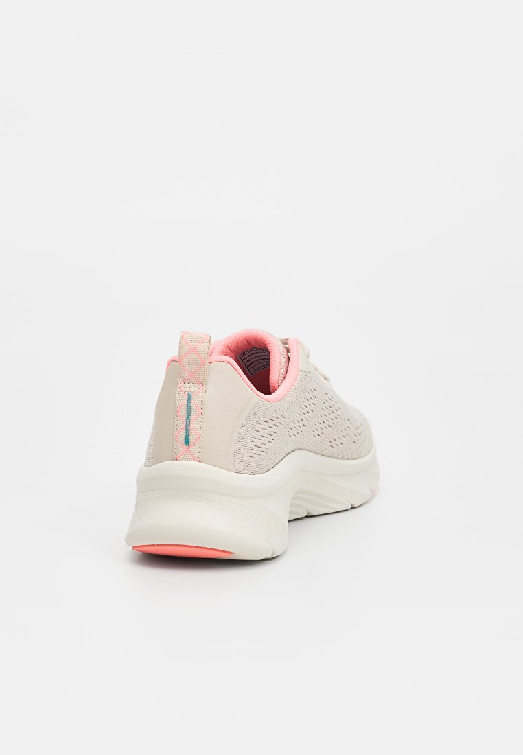 Zapatilla deportiva de color beige claro con parte superior de malla, acentos en rosa, un patrón texturizado y suela blanca gruesa con talón rosa.