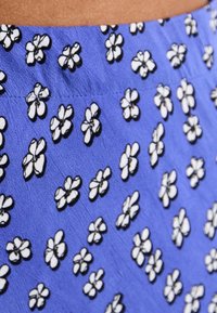 Tissu bleu à texture légère présentant un motif de petites fleurs blanches bordées de noir, réparties uniformément sur toute la surface.