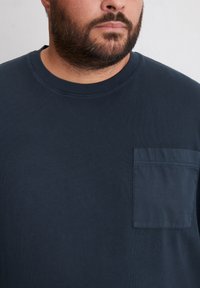 Navyblauwe t-shirt met korte mouwen, een geribbelde textuur, ronde halslijn en een borstzak met een contrasterende stof.