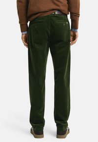 Dunkelgrüne Cordhosen mit einem geraden Bein-Design, ausgestattet mit zwei Gesäßtaschen und einer weichen Textur. Kombiniert mit braunen Schuhen.