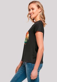 Black cotton t-shirt with short sleeves featuring a colorful circular graphic of mountains and trees. Smooth texture, relaxed fit.