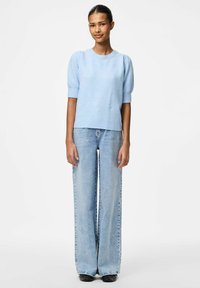 Ljusblå stickad tröja med korta puffärmar, kombinerad med högmidjade, vida ljusblå jeans och svarta skor. Enkel design, utan mönster.