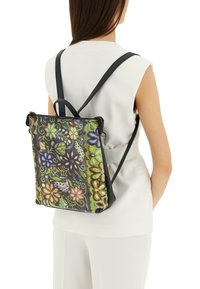 Zaino floreale multicolore realizzato in materiale tessurizzato con dettagli in pelle nera e spallacci regolabili, caratterizzato da vivaci motivi verdi, viola e arancioni.