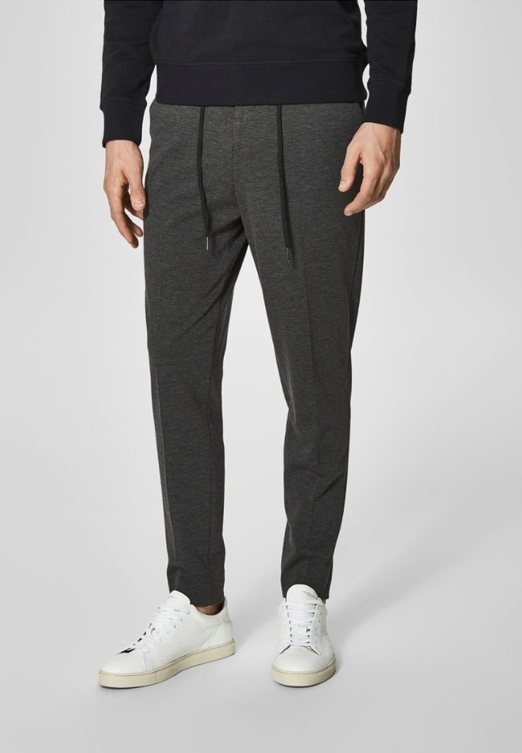 Szare spodnie dresowe z miękkiego materiału z regulowanym paskiem w talii, przednimi kieszeniami i zwężanymi nogawkami, w połączeniu z białymi trampkami.