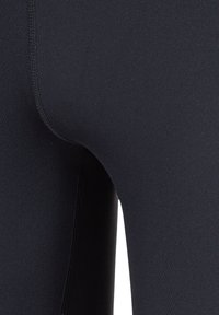 Zwarte leggings gemaakt van rekbare stof, met een gladde textuur en platte naden voor duurzaamheid. Close-up afbeelding benadrukt de pasvorm rond de taille.