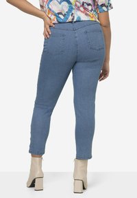 Los jeans skinny de mezclilla azul claro presentan una cintura alta, bolsillos traseros y una textura suave, combinados con botas de tacón cuadrado de color crema.