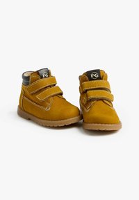 Stivaletti alla caviglia gialli in suede con due cinturini in Velcro regolabili, suole in gomma marrone e dettagli di cucitura a contrasto. Etichetta nera sulla linguetta.