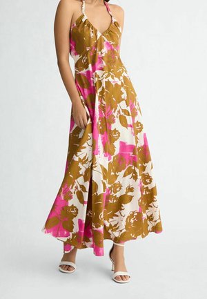 Femme portant une robe sans manches, col en V, longue jusqu'aux chevilles, avec de grands motifs floraux marron et rose et des sandales blanches à talons.