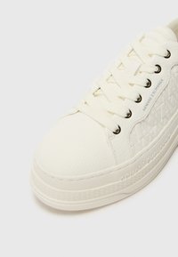 Hvit sneaker med teksturert skinn, flate lisser og logodetaljer. Gummisåle med mønstrede aksenter langs kanten.
