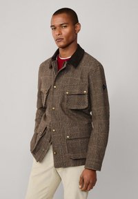 Bruine blazer met een geruite patroon en een donkere kraag, voorzien van borst- en zijzakken, goudkleurige knopen en een getailleerd ontwerp.
