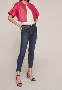 Rosa fuskpälskroppad jacka med vågiga ärmar, ihopparad med mörkblå skinny jeans och svarta klacksandaler.