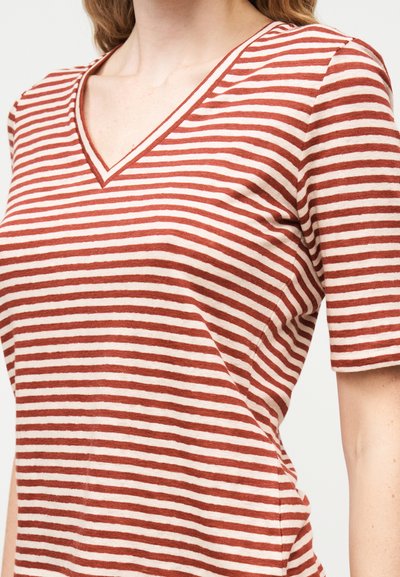 Γυναίκα που φοράει λευκό και σκουροκόκκινο οριζόντια ριγέ μπλουζάκι με V λαιμόκοψη και κοντά μανίκια, εμφανιζόμενη από τους ώμους έως τη μέση.