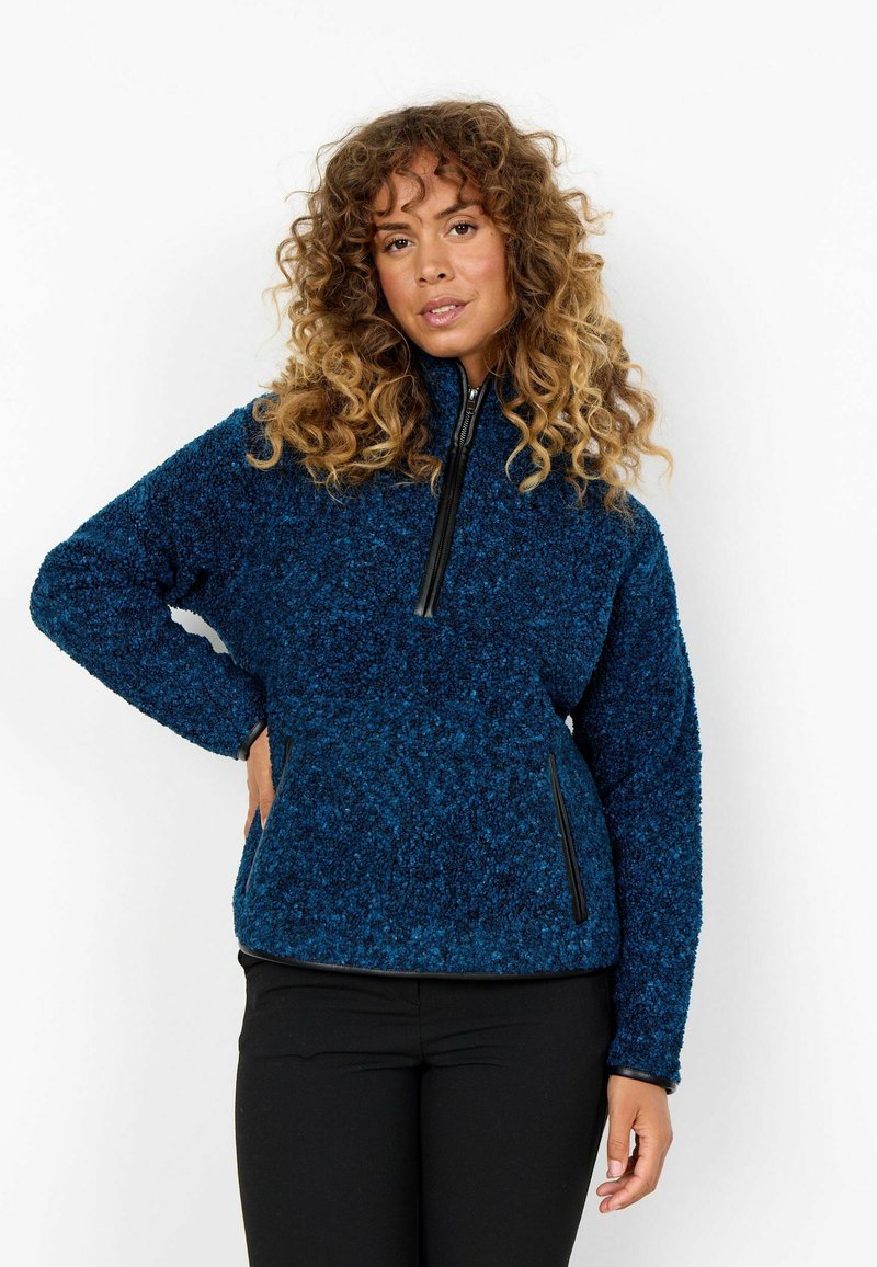 Fleece pulover u tamnoplavoj boji s polu-zip zatvaračem sprijeda. Sadrži dva bočna džepa s crnim zatvaračima i teksturiranu, mekanu tkaninu.