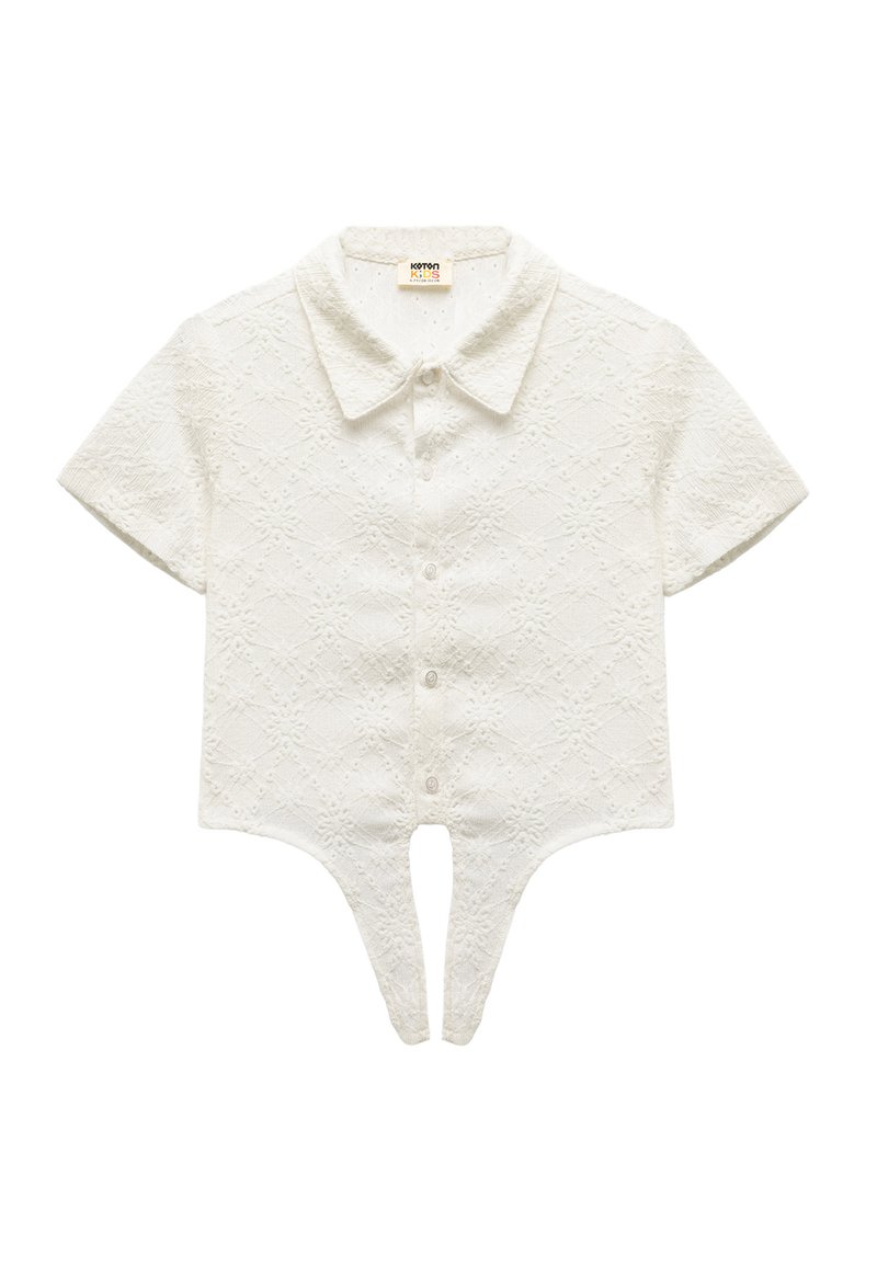 Hvid bluse med korte ærmer og et struktureret diamantmønster. Har en spidse krave og knaplukninger samt et unikt split-hjem-design.