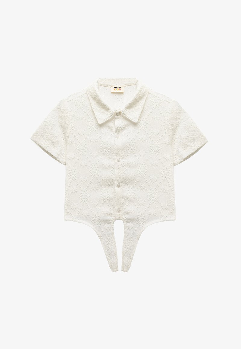 White short-sleeve blouse with a textured, diamond pattern. Features a pointed collar and button closures, with a unique split hem design.