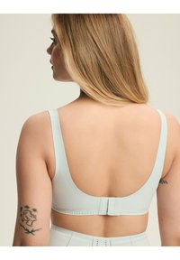 Jasnoniebieski biustonosz z szerokimi ramiączkami, gładką teksturą i niskim tyłem. Posiada zapięcie na haczyk i oczko oraz subtelne perforacje wzdłuż pasa.