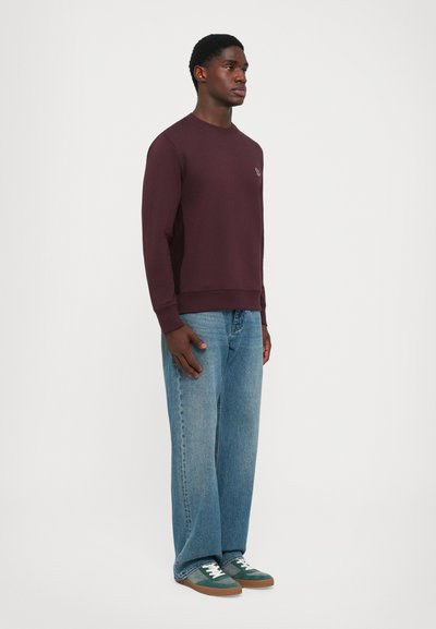 Burgundy sweatshirt, long sleeves, ribbed cuffs, worn with light blue loose-fit jeans and green sneakers with white laces and brown soles.