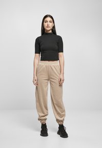 Svart kortärmad croptopp, beige mjuka fleecebyxor med elastiska muddar och linning, i kombination med svarta sneakers. Enkel, avslappnad passform.