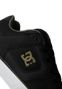 Black sneaker featuring a textured leather upper, fabric elements, a white sole, and a prominent logo in olive green. Lacing system included.