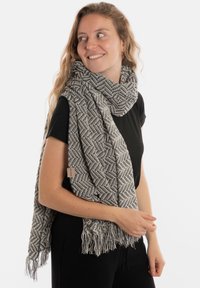 Écharpe tissée noire et blanche avec un motif en chevrons et des bords frangés, drapée autour de l'épaule et du cou.
