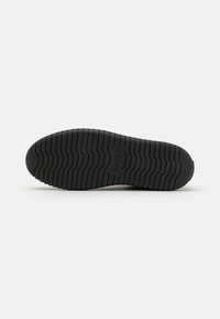 Semelle de chaussure en caoutchouc noir avec des rainures en zigzag et le nom de la marque Bally embossé au centre sur fond blanc.