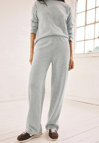 Helehallid loungewear komplekt pehmest kangast; pikkade varrukatega topp ribima kaelusega ja laiad püksid, koos pruuni värvi tossudega.