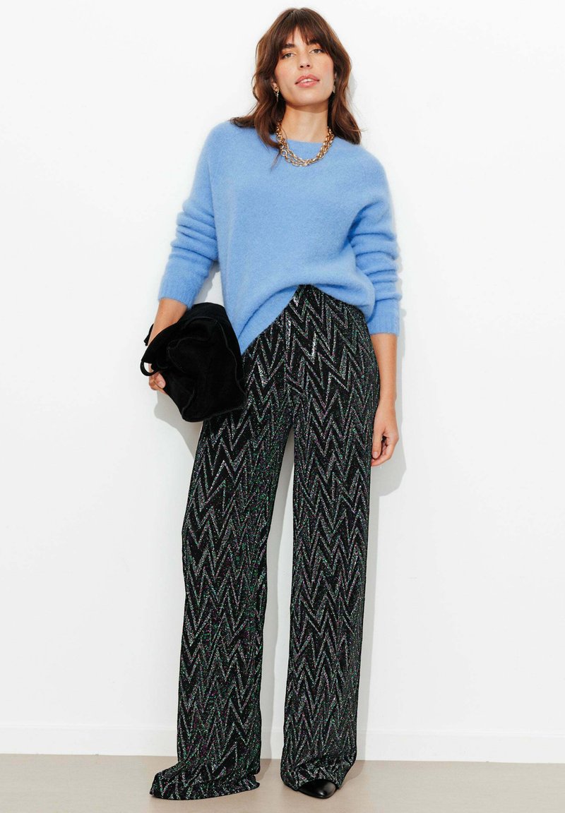 Pull en laine bleu clair à manches longues, associé à un pantalon noir avec un motif zigzag en vert et paillettes argentées. Pochette noire.